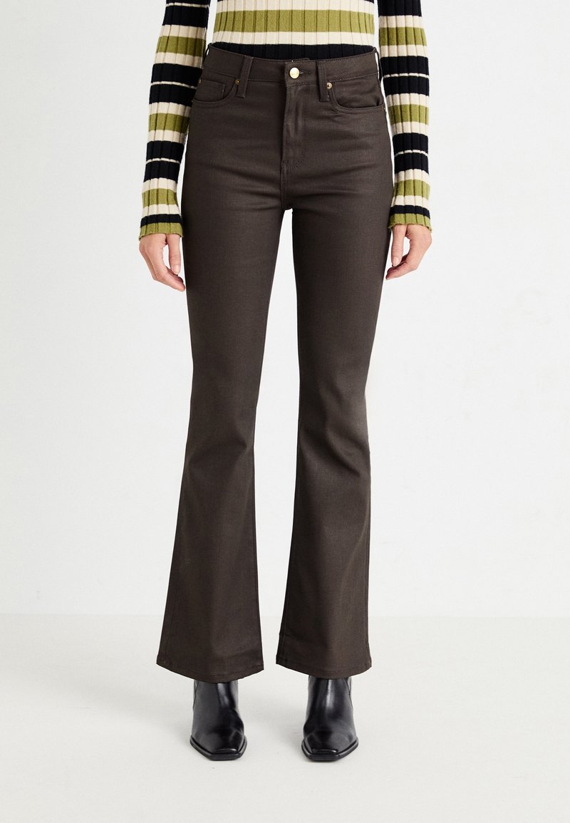 Femme portant un pantalon flare marron foncé ajusté, des bottines noires et un pull côtelé rayé avec des lignes horizontales vertes, blanches et noires.