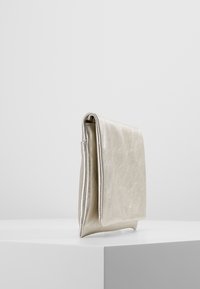 Petit sac pochette en cuir argenté métallique debout sur une surface blanche contre un fond uni.