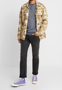 Conjunto informal que incluye una chaqueta beige con estampado, un suéter gris, jeans oscuros y zapatillas altas moradas con suelas y detalles blancos.