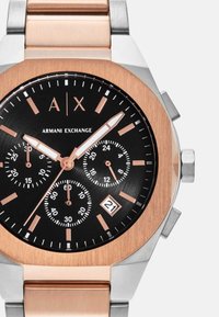 Roosa kuldne ja hõbedane Armani Exchange kell musta kube, kolme aladialiga, kuupäevaaken 4. kohal ning helendavad kellanäidikud ja markerid.