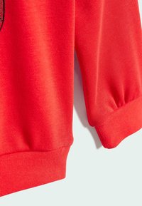 El sudadera roja presenta un tejido texturizado, puños y dobladillo acanalados, con un ajuste ligeramente holgado. Los extremos de las mangas están fruncidos para un aspecto ceñido.