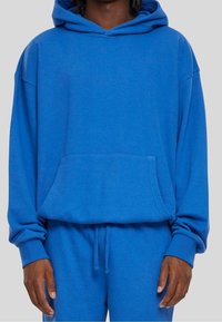 Sudadera con capucha azul, hecha de una tela suave, con un bolsillo frontal. Corte holgado con puños y dobladillo acanalados, presenta un diseño liso sin patrones.