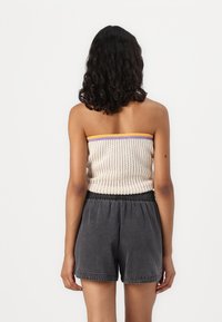 Haut en tricot sans bretelles de couleur crème avec des bords violet et orange, associé à un short noir ample avec une taille élastique.