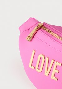 Ροζ τσάντα από συνθετικό δέρμα με χρυστό φερμουάρ και τη λέξη «LOVE» σε χρυσά γράμματα μπροστά, με λεία υφή και στρογγυλεμένο σχήμα.