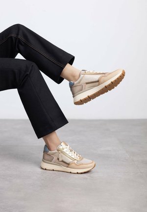 Zapatillas beige y metálicas con tejido texturizado, diseño con cordones y suela gruesa. Presentan una cremallera lateral y detalles en azul contrastante.