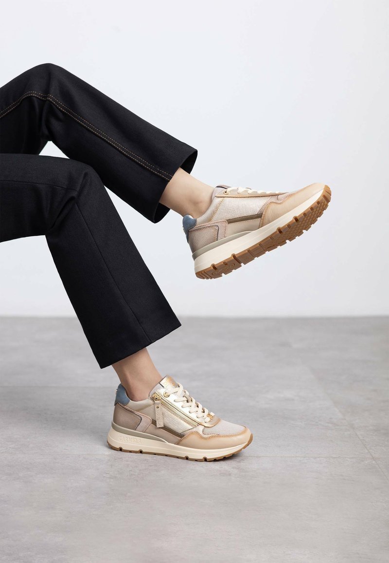Zapatillas beige y metálicas con tejido texturizado, diseño con cordones y suela gruesa. Presentan una cremallera lateral y detalles en azul contrastante.