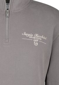 Pull en polaire gris avec un col zippé jusqu'à mi-hauteur. Caractérisé par un logo brodé blanc "Sergio Tacchini" et "Sportivo 1966" sur la poitrine. Texture lisse.