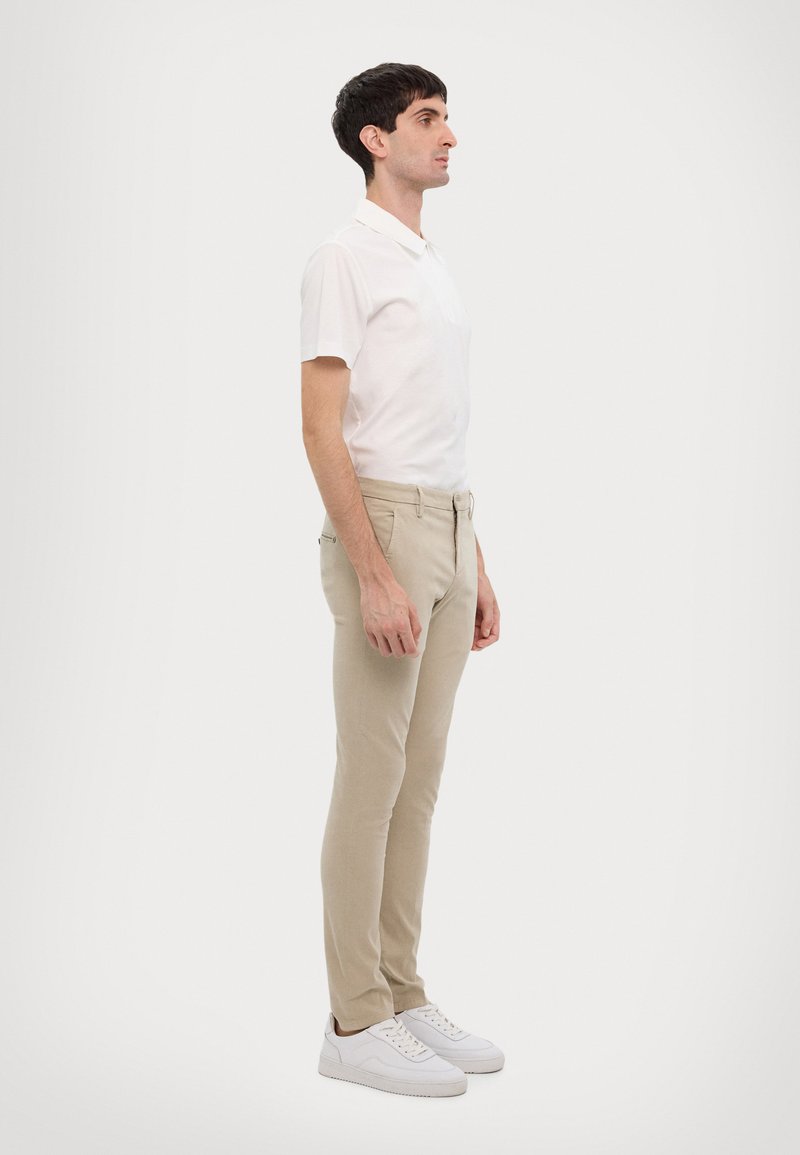 Polo shirt blanc léger associé à un pantalon beige slim-fit et des baskets blanches, avec un col classique et un détail de poche sur le devant.