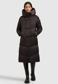 Pitkä, tummanruskea toppatakki, jossa korkea, taitettava kaulus; siinä tikattu kuvio ja mustia metalliosia; yhdistetty polven korkeisiin mustiin saappaisiin.