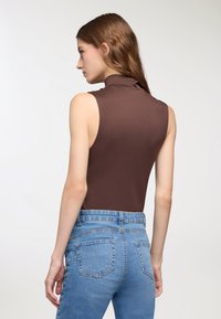 Top senza maniche in turtleneck marrone abbinato a jeans in denim chiaro. Il top presenta una texture liscia; i jeans includono tasche posteriori e una vestibilità classica.