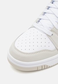 Baskets en cuir gris clair avec un bout perforé blanc, des accents texturés et des lacets blancs ; dotées d'une semelle en caoutchouc avec un motif de rainure subtil.