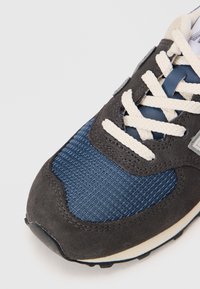 Chaussure de sport avec un dessus en suède texturé gris foncé et en mesh navy, des lacets blancs et une semelle extérieure en caoutchouc noir durable.