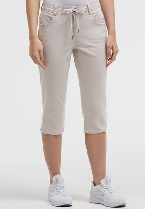 Light beige cropped pants with drawstring waist worn by a standing person, paired with white athletic shoes on a white background.