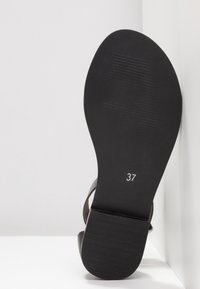 Semelle de sandale plate noire avec le numéro de taille 37 imprimé en blanc, présentant un talon texturé et une semelle avant lisse.