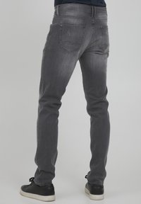 Jeans de mezclilla gris con un ajuste slim, que cuentan con dos bolsillos traseros, un acabado desgastado y detalles acolchados. Acompañados de zapatillas negras.