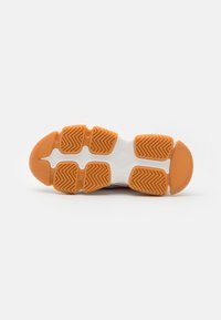 Suela de zapato deportivo con goma naranja y patrón de tracción de espiga, media suela blanca y diseño de talón redondeado y suave.