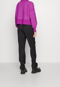 Pull violet court en maille texturée avec ourlet côtelé, associé à un pantalon noir à coupe droite avec un détail subtil de poche arrière.