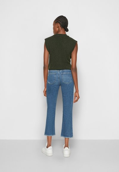 Top verde cropped sem mangas, jeans azuis de cintura alta com bainha desfiada e ténis brancos. Design simples e casual com um ajuste descontraído.