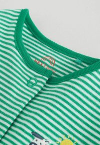 Detský overal s zelenými a bielymi pruhmi, zapínaný na patentky, s čiastočným potlačením slnka a zvierat pri spodnej časti.