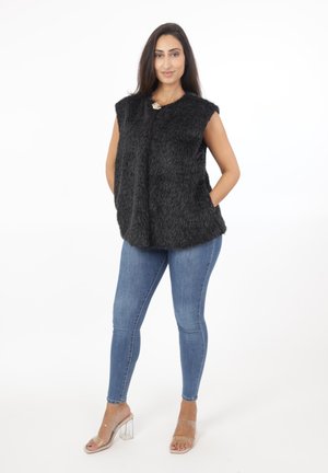 Sort faux fur vest med løsts fit, rund halsudskæring og guld broche detalje. Sammen med blå skinny jeans og klare hælede mules.