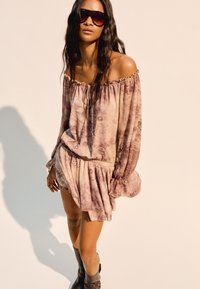 Schulterfreies, langärmliges Kleid aus weichem, strukturiertem Stoff mit einem rosa und cremefarbenen Blumenmuster; elastischer Taillenbund, Rüsche am Saum, kombiniert mit einer Sonnenbrille.