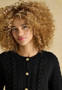 Czarny dziany kardigan z wzorem w warkocze i okrągłym dekoltem. Złote guziki podkreślają przód, uwydatniając teksturę i design.