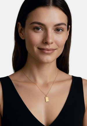 Junge Frau mit glattem dunklem Haar, die ein schwarzes ärmelloses Oberteil und eine rechteckige goldene Anhängerkette trägt, lächelt sanft.