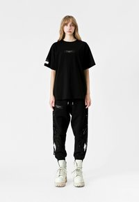Camiseta negra oversize y pantalones de chándal con diseño de plumas en negro brillante. Botas blancas con cordones, que cuentan con una suela resistente, completan el look.