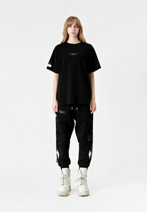 Camiseta negra oversize y pantalones de chándal con diseño de plumas en negro brillante. Botas blancas con cordones, que cuentan con una suela resistente, completan el look.