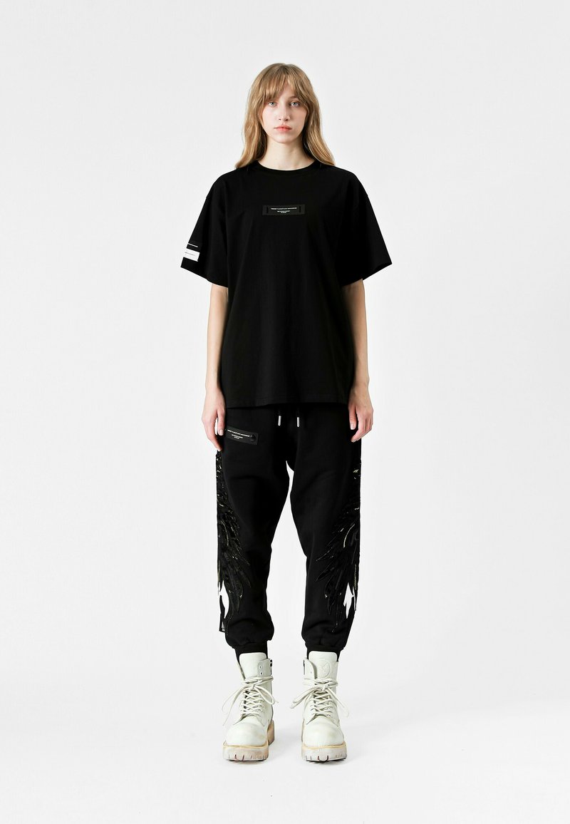 Camiseta negra oversize y pantalones de chándal con diseño de plumas en negro brillante. Botas blancas con cordones, que cuentan con una suela resistente, completan el look.