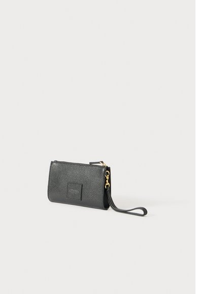 Pochette poignet texturée noire avec une fermeture éclair et une sangle dorées sur un fond blanc.