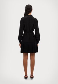 Melna plīšu kleita ar garām piedurknēm, apkakles ir, un ar jostu viduklī. Gluda tekstūra ar paplatinātu svārku, kas sasniedz vidusceli.