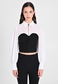 Top nero tagliato con scollatura a forma di cuore e maniche lunghe bianche. Caratterizzato da un colletto con dettaglio di bottone metallico. Tessuto morbido.
