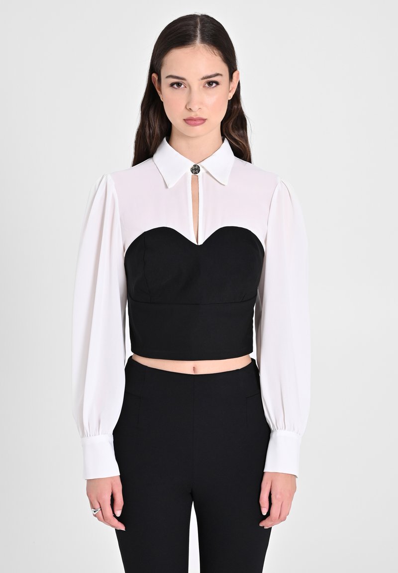 Top nero tagliato con scollatura a forma di cuore e maniche lunghe bianche. Caratterizzato da un colletto con dettaglio di bottone metallico. Tessuto morbido.