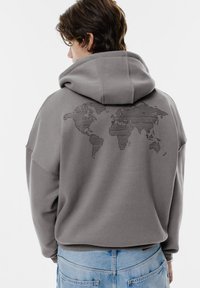 Grå hoodie med en stor, svart linjetecknad världskarta grafisk bild på baksidan. Har en avslappnad passform och huva, med ribbade ärmslut och nederkant.