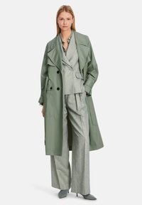 Green trench coat over gray suit with a tailored jacket and wide-leg trousers. The coat features large black buttons and prominent lapels.
