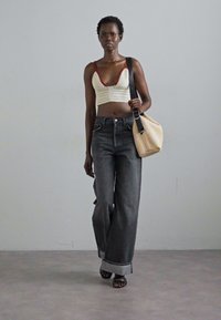 Top corto all'uncinetto con rifiniture rosse, abbinato a jeans neri a vita alta e gamba larga e a una borsa beige testurizzata. Sandali flat completano il look.