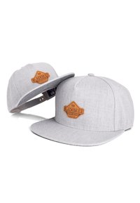 Grå stof snapback kasket med en flad skygge, der har et tekstureret brunt lædermærke prægede med "BLACKSKIES." To kasketter vist.