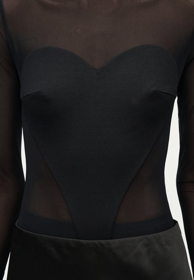 Μαύρο διάφανο τοπ με μακριά μανίκια, στερεό μαύρο μπούστο σε σχήμα καρδιάς και λεία φούστα στη μέση.