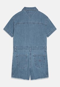 Světle modrý denimový overal s krátkým rukávem, límečkem, našitými kapsami na zádech a třepeným lemem. Na zádech je vodorovný šev.