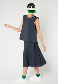 Vestido sin mangas azul marino con silueta acampanada, combinado con zapatillas blancas y calcetines verdes. Los accesorios incluyen una visera verde y blanca.