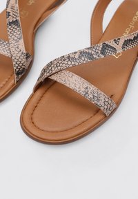 Sandalias planas marrones con correas cruzadas en un patrón de serpiente, con una planta de cuero suave y detalles texturizados en las correas.