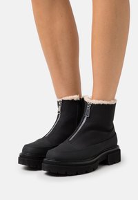 Zwarte enkellaarsjes met ritssluiting en een met bont gevoerde kraag. Voorzien van een dikke, robuuste zool voor extra grip en duurzaamheid.