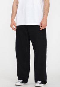 Sorte denimbukser med en løs pasform og lige ben. Bæret med en hvid t-shirt og sorte sneakers, der viser en enkel, afslappet stil.