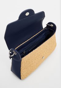 Borsa in paglia intrecciata con parte superiore in pelle blu navy, chiusura magnetica e hardware in argento. L'interno presenta una tasca con zip aggiuntiva e rivestimento liscio.