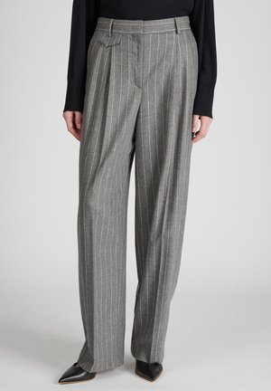 Grau melierte Wollhose mit vertikalen weißen Nadelstreifen, hoher Taille, gefältelter Vorderseite und weitem Bein. Getragen mit schwarzen spitzen Schuhen.