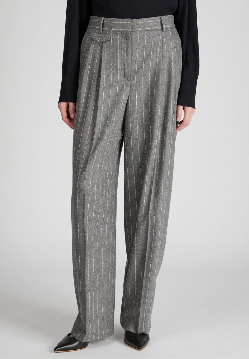 Pantaloni di lana grigi con righe verticali bianche, vita alta, parte anteriore plissettata e gambe larghe. Indossati con scarpe nere con punta a punta.