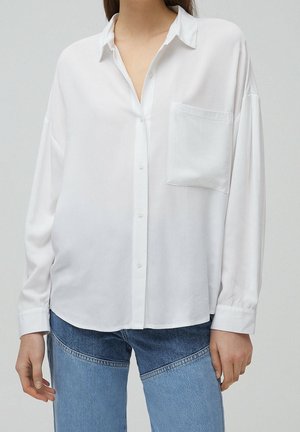 Woman wearing loose white button-up shirt with chest pocket paired with two-tone blue jeans, shown from neck to hips.