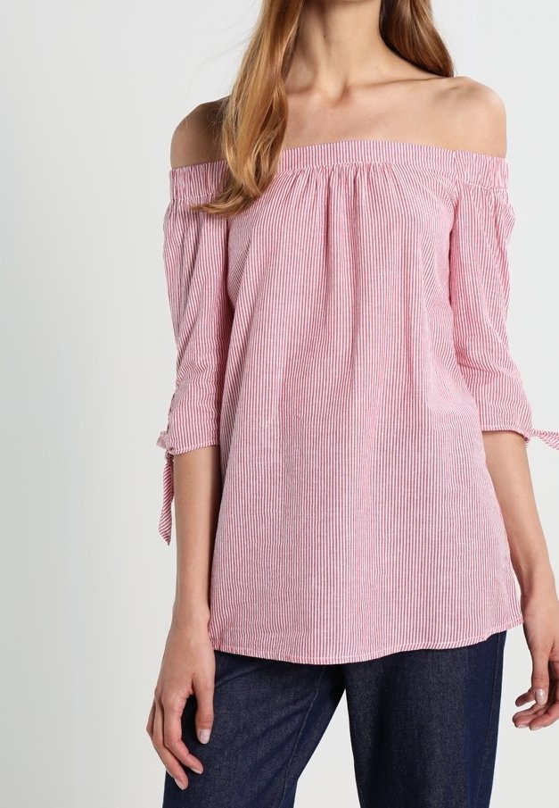 Donna che indossa una blusa a righe rosa e bianca senza spalle con maniche a 3/4 annodate ai gomiti e jeans blu scuro.