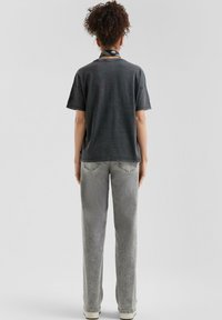 Donkergrijze t-shirt met korte mouwen en een ontspannen pasvorm, gecombineerd met lichtgrijze wijde broek en een patroon sjaal om de nek.